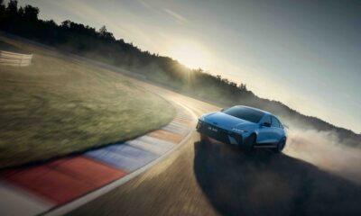 A Hyundai IONIQ 6 N powerslides around a racetrack corner at sunset, kicking up smoke and showcasing its performance handling.
