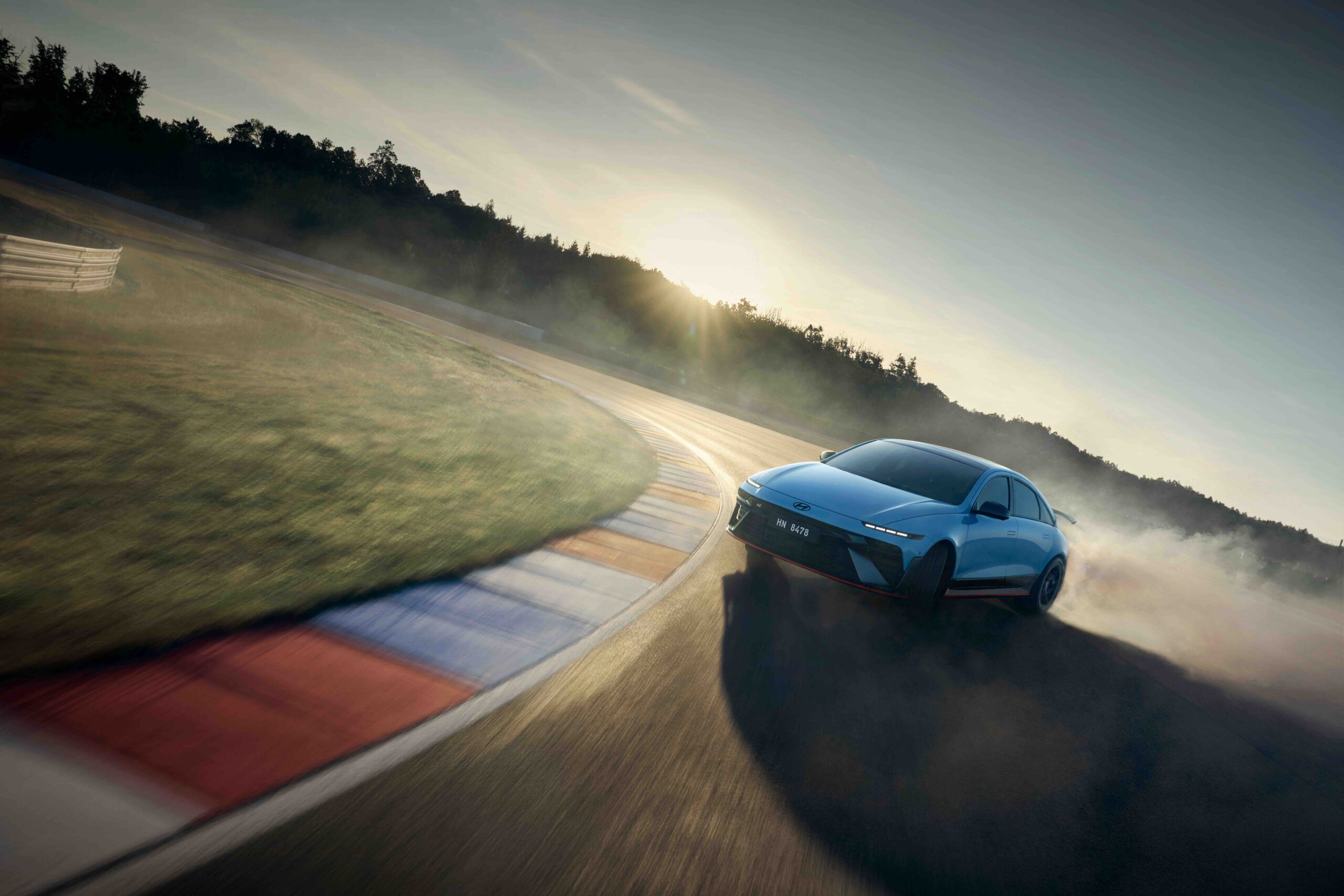 A Hyundai IONIQ 6 N powerslides around a racetrack corner at sunset, kicking up smoke and showcasing its performance handling.