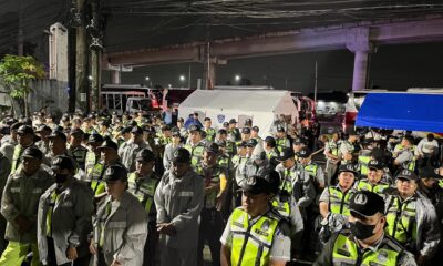 Dozens of uniformed traffic enforcers in reflective vests and rain gear gather at night under bright lights, preparing for deployment ahead of SONA 2025.