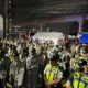 Dozens of uniformed traffic enforcers in reflective vests and rain gear gather at night under bright lights, preparing for deployment ahead of SONA 2025.