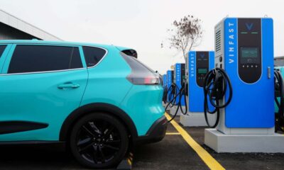 A turquoise VinFast electric vehicle parked and charging at a row of V-Green EV charging stations.