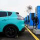 A turquoise VinFast electric vehicle parked and charging at a row of V-Green EV charging stations.