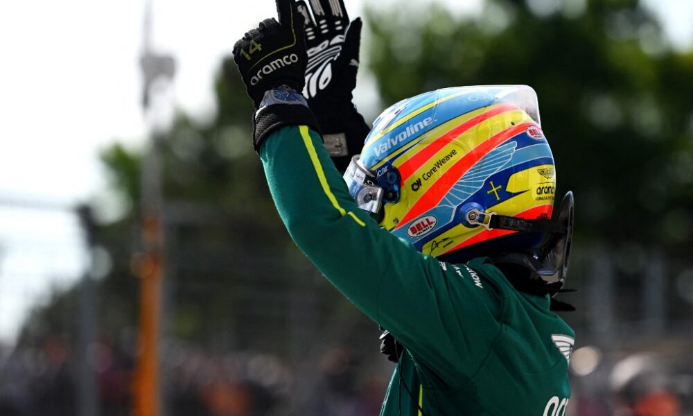 Fernando Alonso raises his hands in celebration while wearing his Aston Martin racing suit and helmet during the Hungarian Grand Prix weekend.