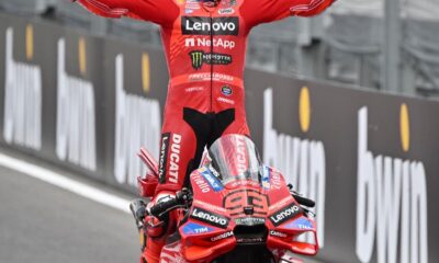 Marc Marquez celebrates his Austrian MotoGP victory on his Ducati, arms wide open while standing on the bike.