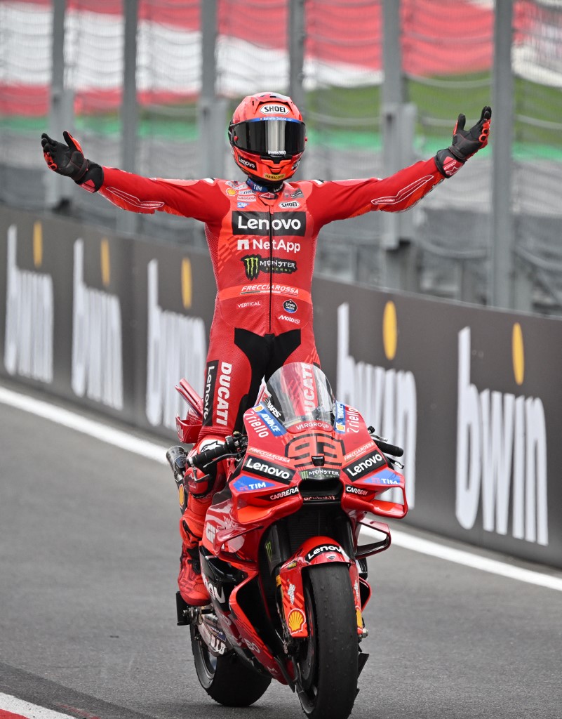 Marc Marquez celebrates his Austrian MotoGP victory on his Ducati, arms wide open while standing on the bike.