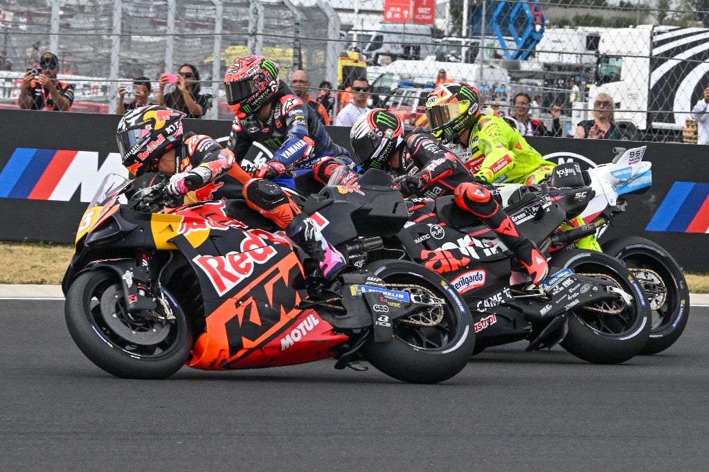 MotoGP riders tightly packed at the start of the Hungarian Sprint race, with KTM, Yamaha, and Aprilia bikes side by side in action.