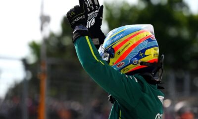 Fernando Alonso raises his hands in celebration while wearing his Aston Martin racing suit and helmet during the Hungarian Grand Prix weekend.