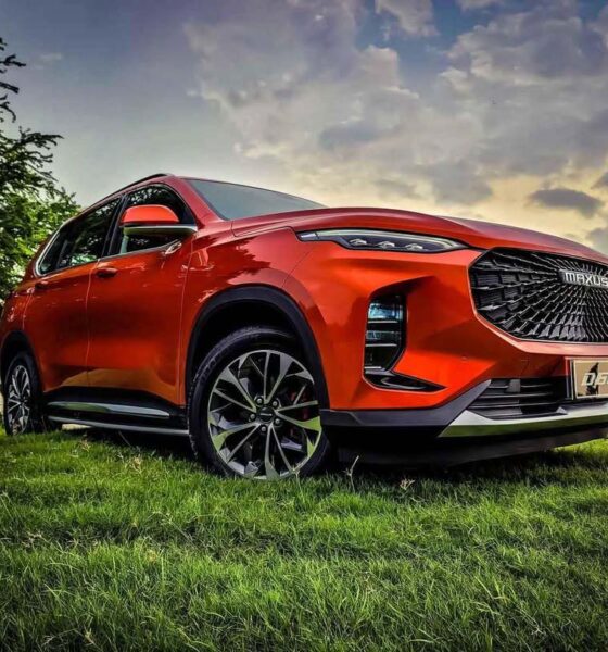 A striking red Maxus D60 SUV parked on a grassy field under a dramatic sunset sky.