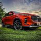 A striking red Maxus D60 SUV parked on a grassy field under a dramatic sunset sky.