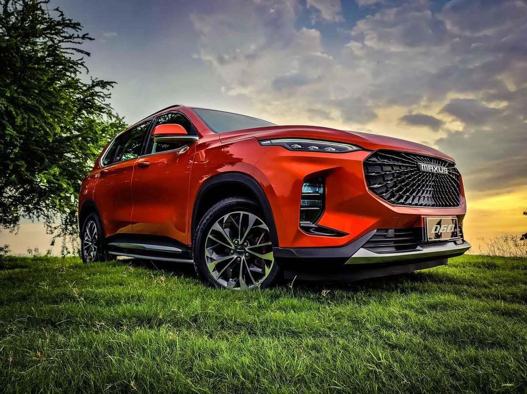 A striking red Maxus D60 SUV parked on a grassy field under a dramatic sunset sky.