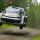Toyota GR Yaris Rally1 airborne on a forest stage during Rally Finland, showcasing high-speed action and precision driving.