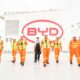 A group of Filipino seafarers and crew members in orange coveralls and safety vests walk on the deck of a BYD roll-on/roll-off vessel, with the large BYD logo visible in the background.