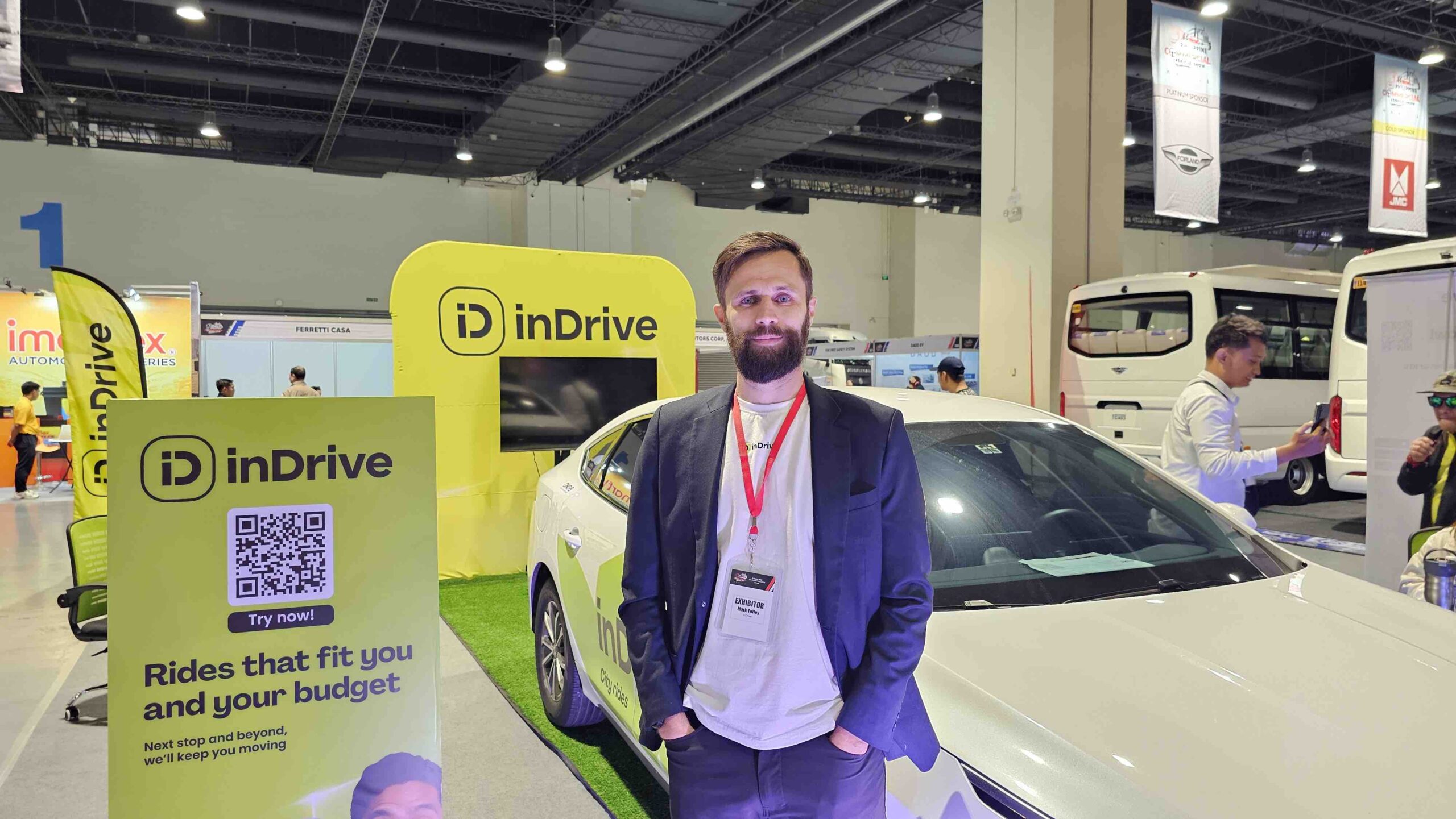 inDrive Regional Director Mark Tolley stands at the inDrive booth during the Philippine Commercial Vehicle Show 2025, with a white inDrive-branded car and promotional signage in the background.