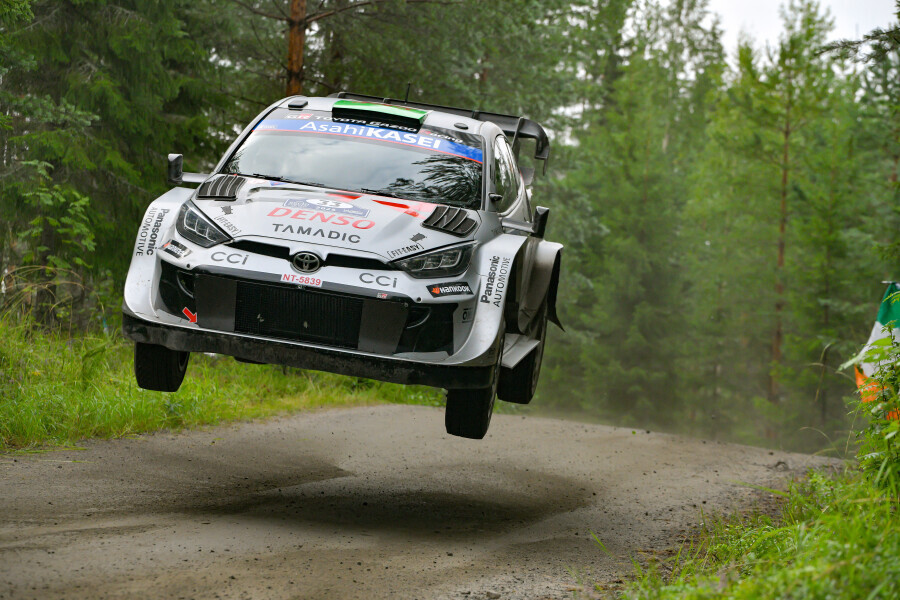 Toyota GR Yaris Rally1 airborne on a forest stage during Rally Finland, showcasing high-speed action and precision driving.