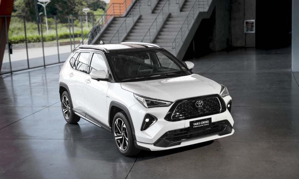 White Toyota Yaris Cross SE Hybrid Electric Vehicle displayed indoors with sporty black accents and alloy wheels.