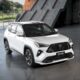 White Toyota Yaris Cross SE Hybrid Electric Vehicle displayed indoors with sporty black accents and alloy wheels.