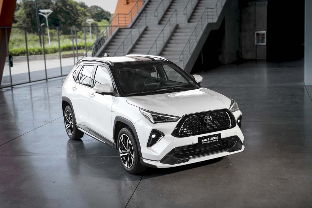 White Toyota Yaris Cross SE Hybrid Electric Vehicle displayed indoors with sporty black accents and alloy wheels.