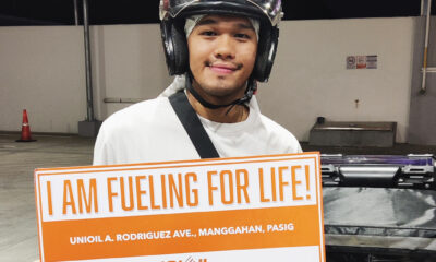 A smiling motorcycle rider wearing a helmet holds a sign that reads "I AM FUELING FOR LIFE!" at a Unioil station in Pasig.