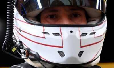 Close-up of a Formula 1 driver wearing a white Cadillac-branded racing helmet with a reflective visor.