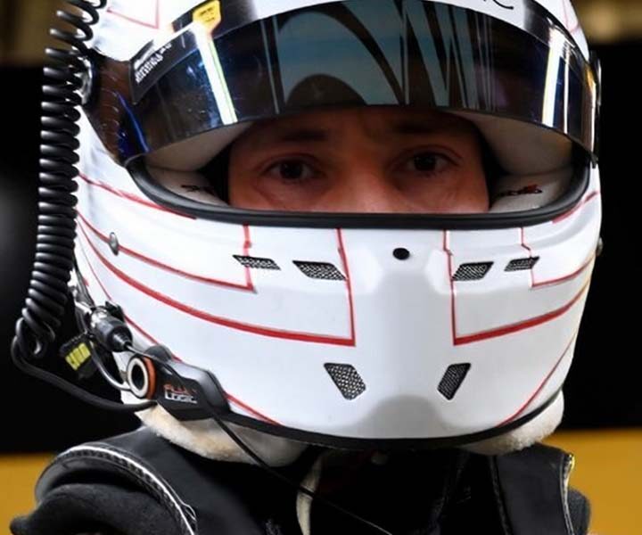 Close-up of a Formula 1 driver wearing a white Cadillac-branded racing helmet with a reflective visor.