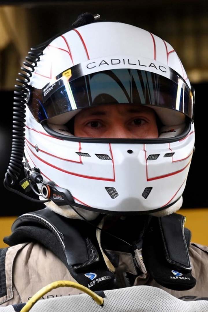 Close-up of a Formula 1 driver wearing a white Cadillac-branded racing helmet with a reflective visor.