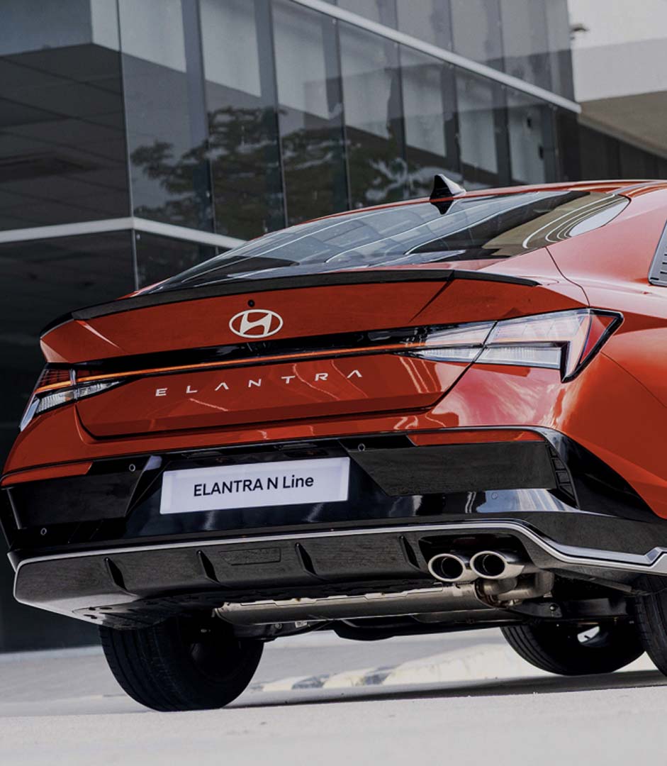 Rear view of the Hyundai Elantra N Line in red, showcasing its sporty bumper, dual exhausts, and bold taillight design.