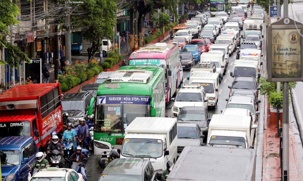 Heavy traffic congestion in Metro Manila with buses, cars, trucks, and motorcycles lined up on a rainy day.