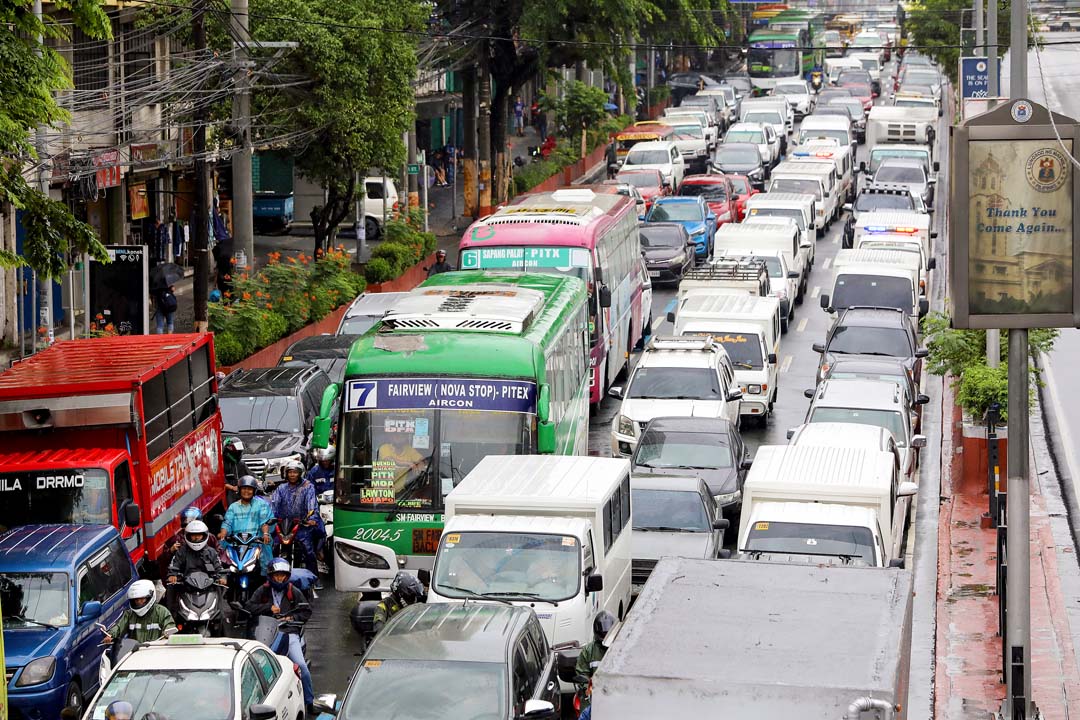 Heavy traffic congestion in Metro Manila with buses, cars, trucks, and motorcycles lined up on a rainy day.
