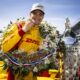 Alex Palou celebrates in victory lane wearing a champion’s cap and floral wreath, standing beside the Borg-Warner Trophy after winning the Indianapolis 500.