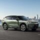 Lynk & Co 08 EM-P plug-in hybrid SUV in Mineral Green driving on a city road with skyline and waterfront in the background.
