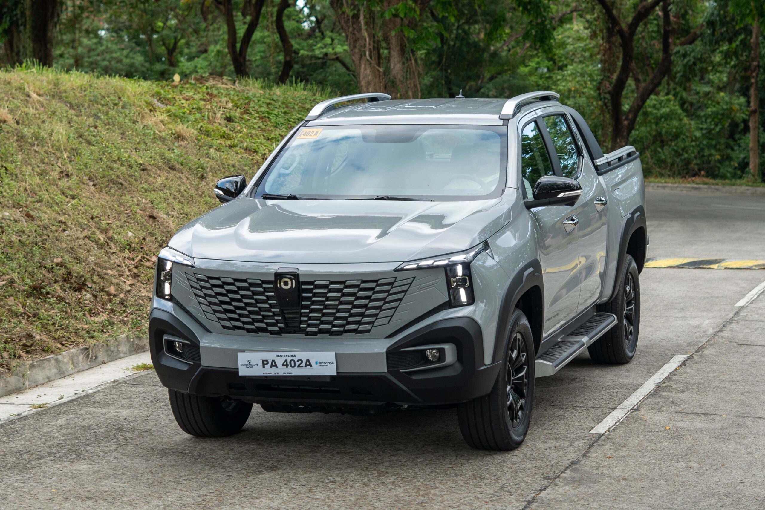 Front view of a gray Changan Nevo Hunter K50 range-extended electric pickup truck parked on a concrete road beside a grassy hillside.