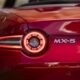 Close-up of the rear taillight and badge of a red Mazda MX-5 sports car.