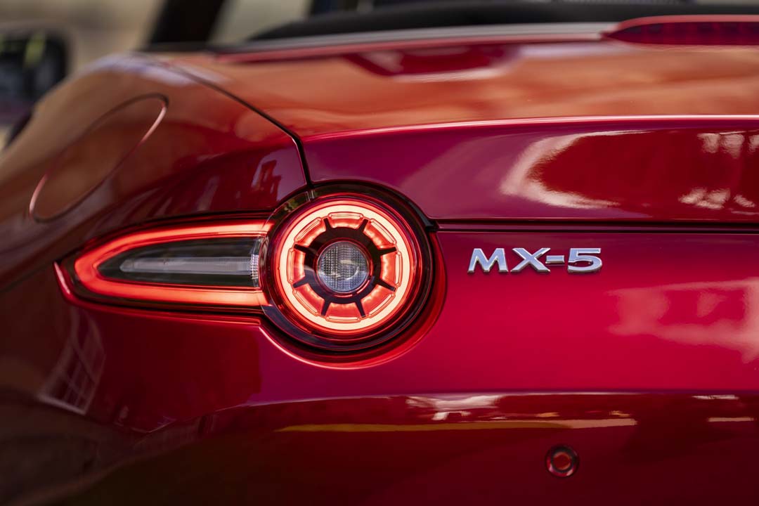 Close-up of the rear taillight and badge of a red Mazda MX-5 sports car.
