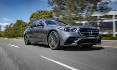A silver Mercedes-Benz luxury sedan driving on a sunny road, captured from a low front-side angle.