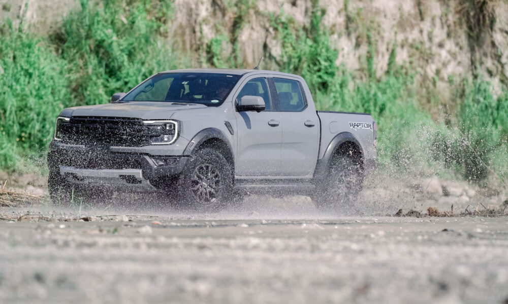 A Ford Ranger Raptor 3.0L V6 drives through a muddy off-road trail, splashing water as it powers forward.