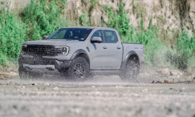 A Ford Ranger Raptor 3.0L V6 drives through a muddy off-road trail, splashing water as it powers forward.