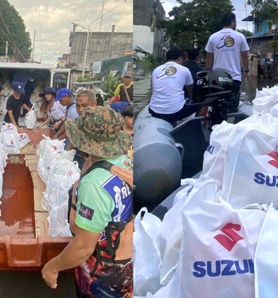 Volunteers and rescue teams use Suzuki-powered boats to deliver white relief bags labeled with the Suzuki logo to flood-affected residents in a submerged neighborhood.