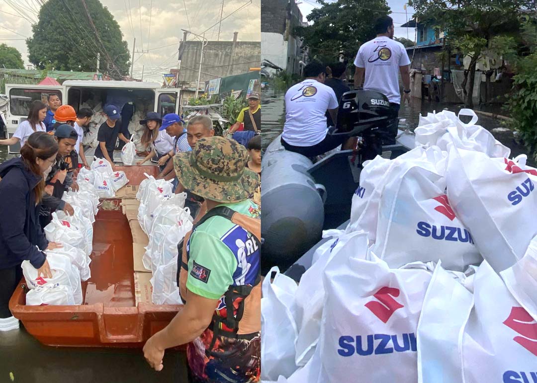 Volunteers and rescue teams use Suzuki-powered boats to deliver white relief bags labeled with the Suzuki logo to flood-affected residents in a submerged neighborhood.