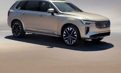 A gold Volvo XC90 Plug-in Hybrid SUV parked under soft daylight, showcasing its modern design and signature Thor’s Hammer LED headlights.