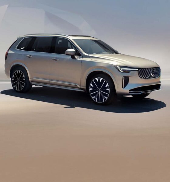 A gold Volvo XC90 Plug-in Hybrid SUV parked under soft daylight, showcasing its modern design and signature Thor’s Hammer LED headlights.