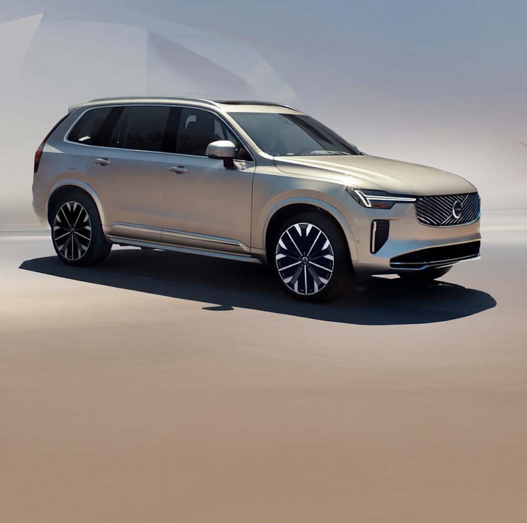 A gold Volvo XC90 Plug-in Hybrid SUV parked under soft daylight, showcasing its modern design and signature Thor’s Hammer LED headlights.
