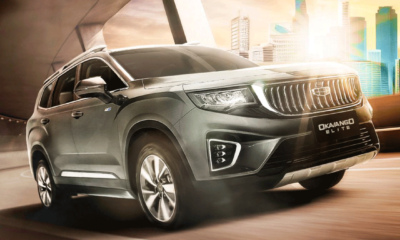 A Geely Okavango Elite SUV driving on an urban road with the city skyline in the background.