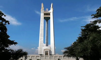 A clear daytime view of the Quezon Memorial Circle monument in Quezon City, framed by trees and a bright blue sky.