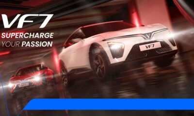 Two VinFast VF 7 electric SUVs—one in red, one in white—racing through a sleek, futuristic tunnel under dramatic red lighting, with motion blur emphasizing speed and power.