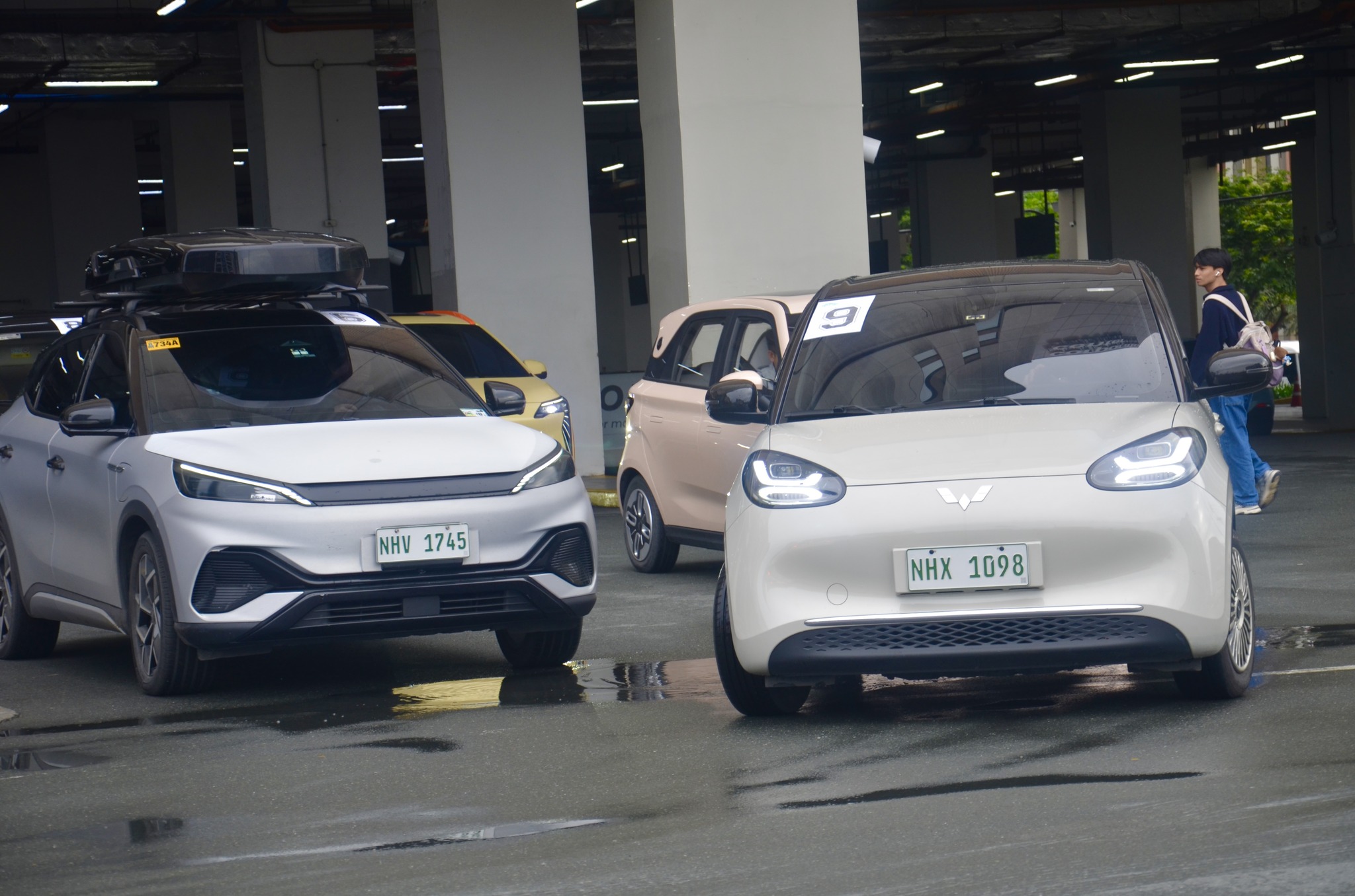 A lineup of electric vehicles, including a BYD crossover and a Wuling compact EV, parked in an urban lot during a Philippine EV industry event.