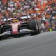 Lewis Hamilton driving his Ferrari F1 car during a race weekend, with a packed grandstand of fans in the background.
