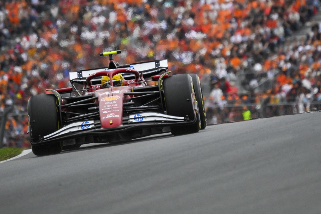 Lewis Hamilton driving his Ferrari F1 car during a race weekend, with a packed grandstand of fans in the background.