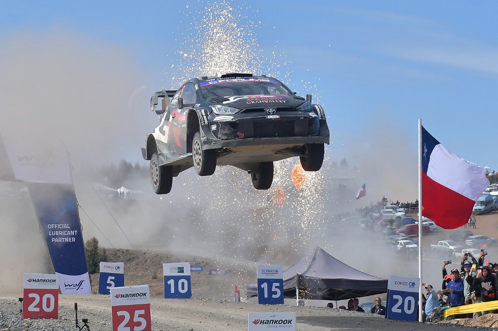 Sebastien Ogier’s Toyota Yaris Rally1 car airborne during a jump at the Rally of Chile, with sparks flying and the Chilean flag in the background.