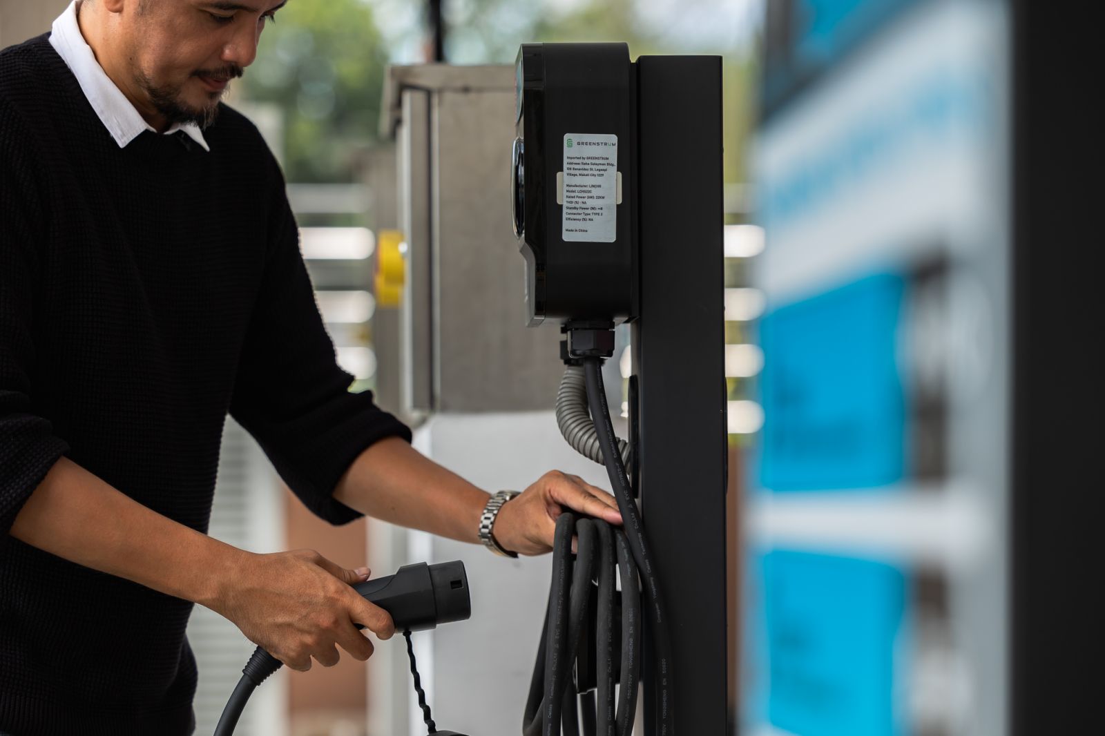 A man prepares an electric vehicle charging cable at an ACMobility charging station in the Philippines.