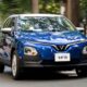 Blue VinFast VF 5 electric crossover driving on a city street with trees and buildings in the background.